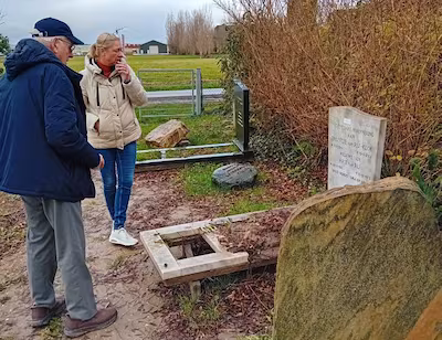 teun-kweekel-en-raadslid-esther-mensink-kijken-naar-de-grafstenen-en-omhulsel-die-bij-een-heg-zijn-n.avif