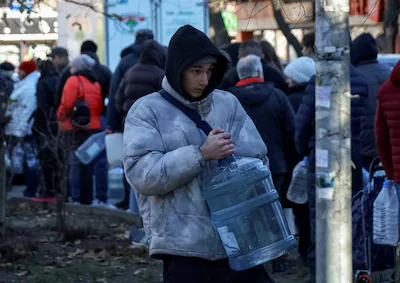 file-photo-a-man-carries-a-can-with-water-as-people-stand-in-line-to-fill-up-bottles-with-fresh-drin.webp