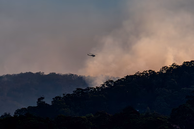kurri-kurri-australia-december-06-a-waterbombing-helicopter-is-seen-flying-over-the-fast-moving-bush.avif