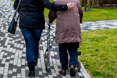 2018-04-04-10-59-35-illustratie-een-bejaarde-vrouw-loopt-met-een-rollator-in-de-tuin-van-een-verzorg.webp