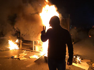 a-protester-flashes-a-victory-sign-in-front-of-a-fire-during-a-demonstration-in-shiraz-iran-on-janua.webp