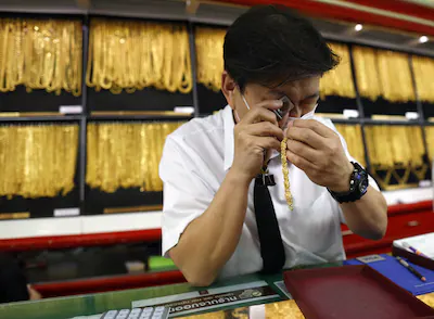 epa12667153-a-goldsmith-examines-gold-ornament-trading-by-a-customer-at-hua-seng-heng-gold-shop-in-b.webp