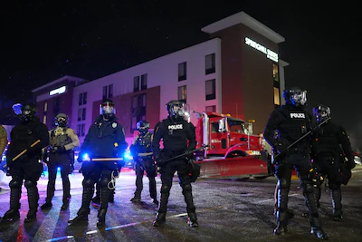 law-enforcement-officers-stand-during-a-protest-outside-springhill-suites-and-residence-inn-by-marri.webp