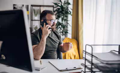 man-talking-on-mobile-phone-while-working-on-the-computer-at-home-office.avif