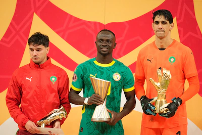 morocco-s-brahim-abdelkader-diaz-left-holds-the-trophy-for-the-best-score-senegal-s-sadio-mane-cente.webp
