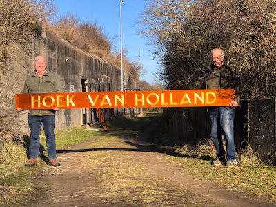 vrijwilligers-jan-valk-links-en-henk-van-ruijven-rechts-met-het-marinebord-hoek-van-holland-voor-bun.avif
